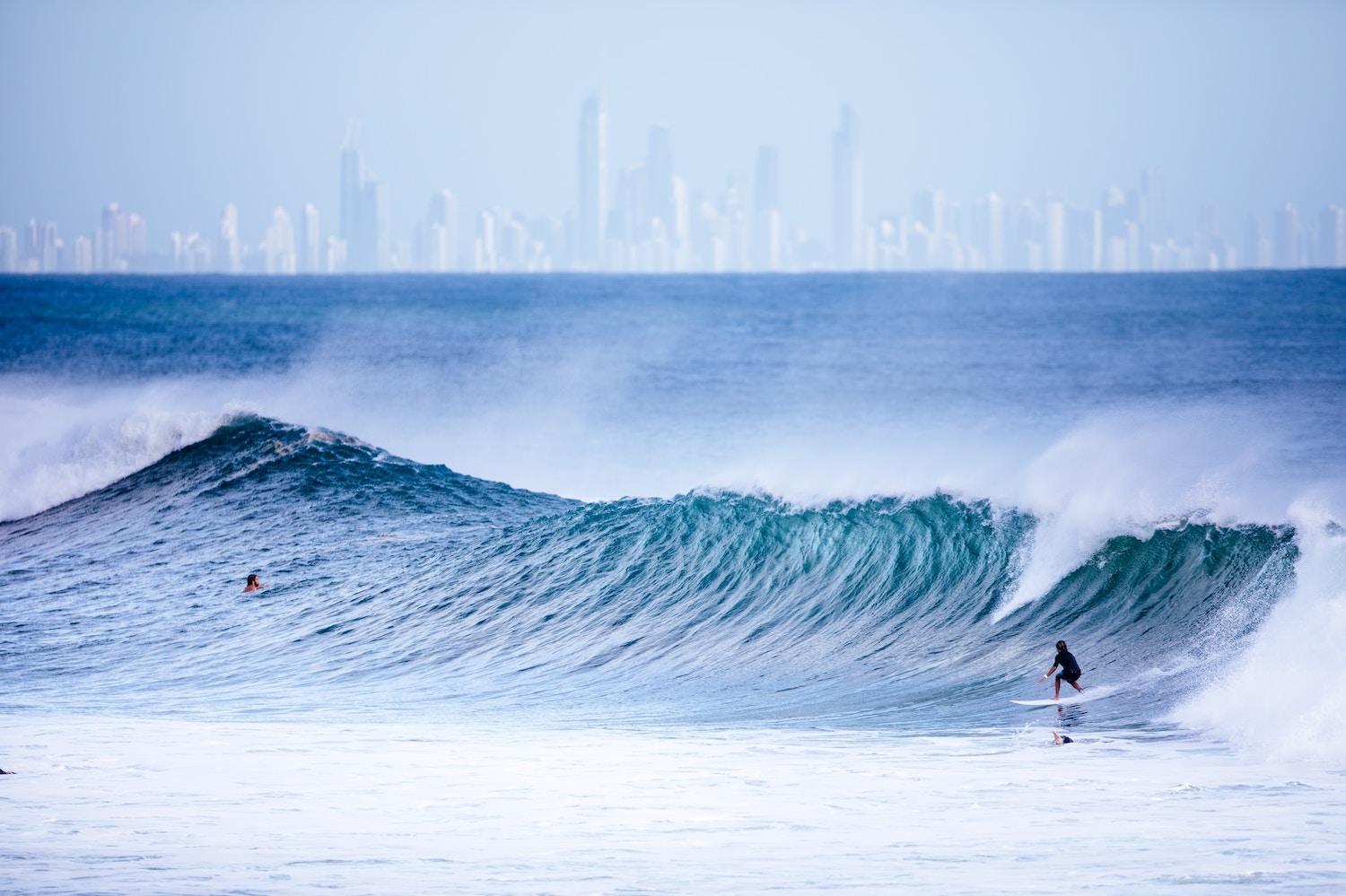 people surfing in the ocean with city skyline in the background - gold coast australia - technology to turn seawater into green hydrogen